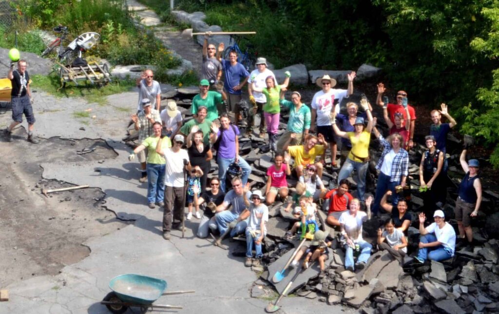 Looking down onto a group of people with shovels which broken concrete beneath then who are waving at the camera and happy