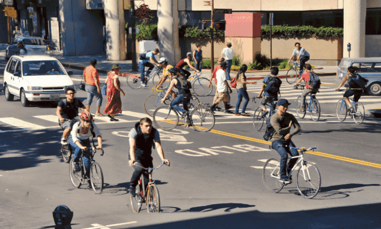 A busy intersection on a city road with many cyclists and a car