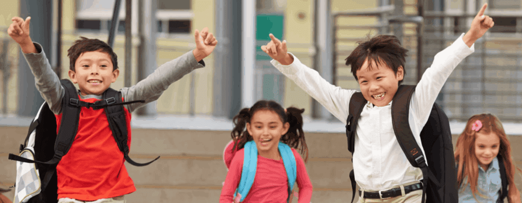 Four school children with backpacks on leaving their school building with smiling faces
