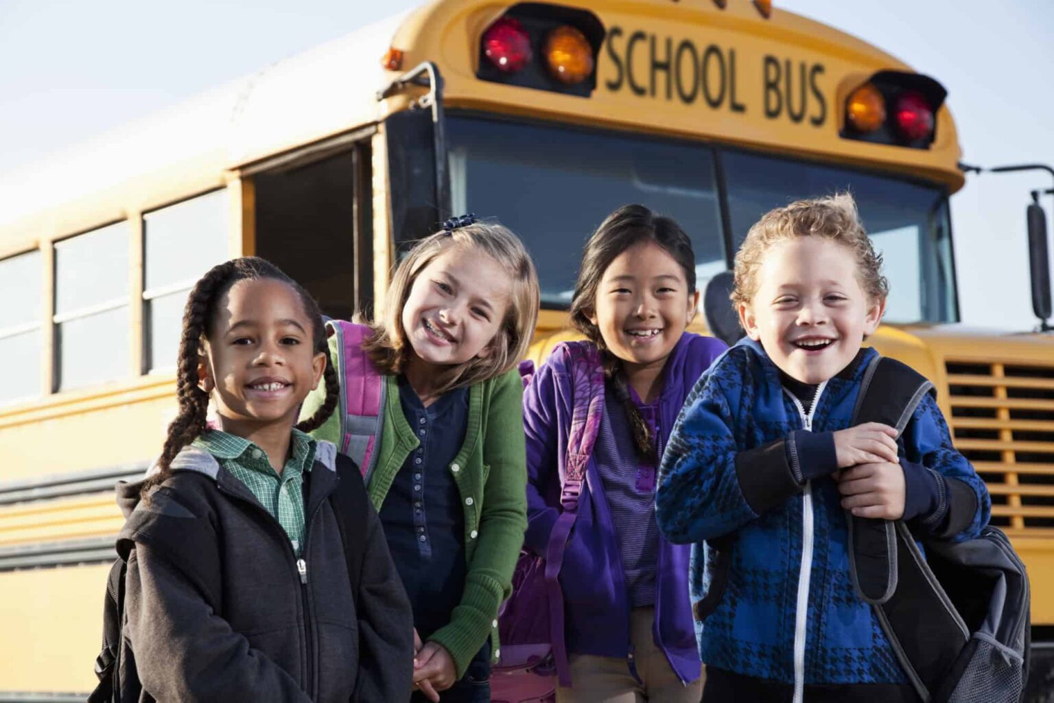 Multi-ethnic children standing in front of school bus.