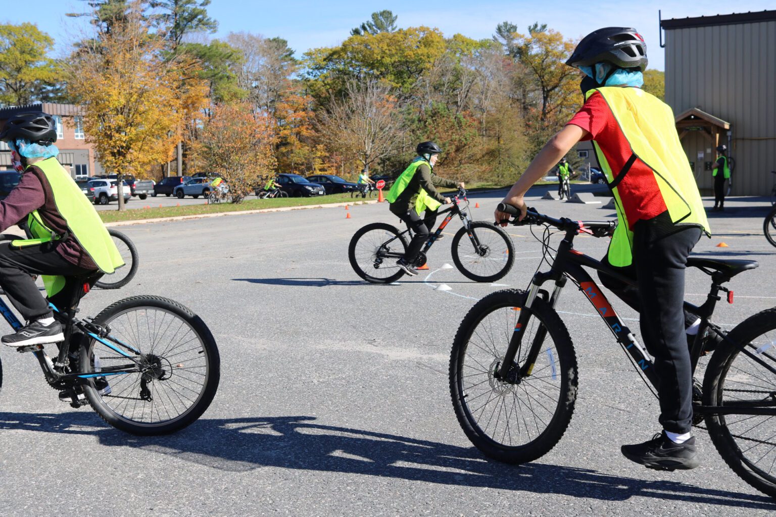 Three grade school-aged kids wearing safety vests and bike helmets maneuvering around small pylons in a school yard