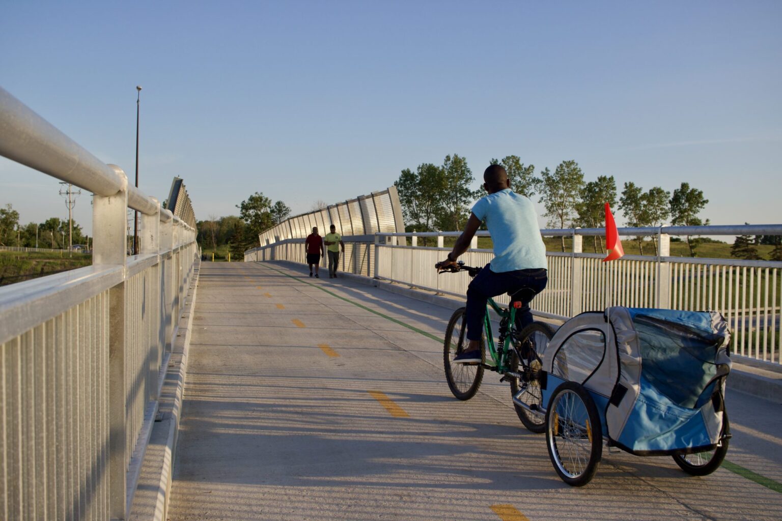 A man cycling with a child carrier over a bridge that has both cycling and pedestrian lanes