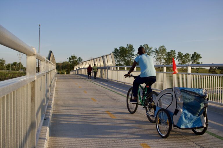 A man cycling with a child carrier over a bridge that has both cycling and pedestrian lanes