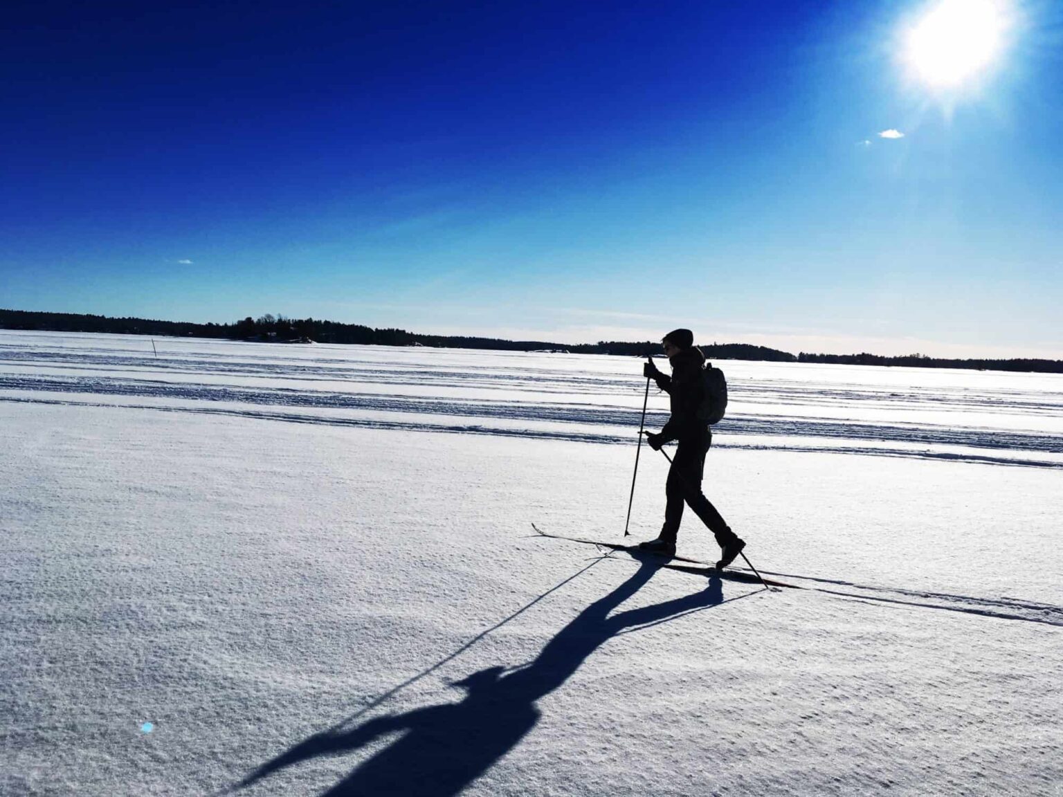 A person cross country skiing on a snow covered field on a bright sunny day.