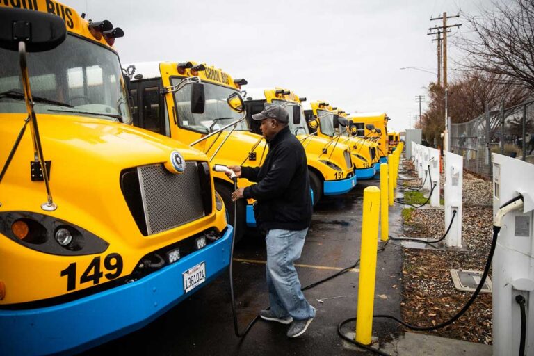 operator plugging in an electric school bus with additional buses in background charging.