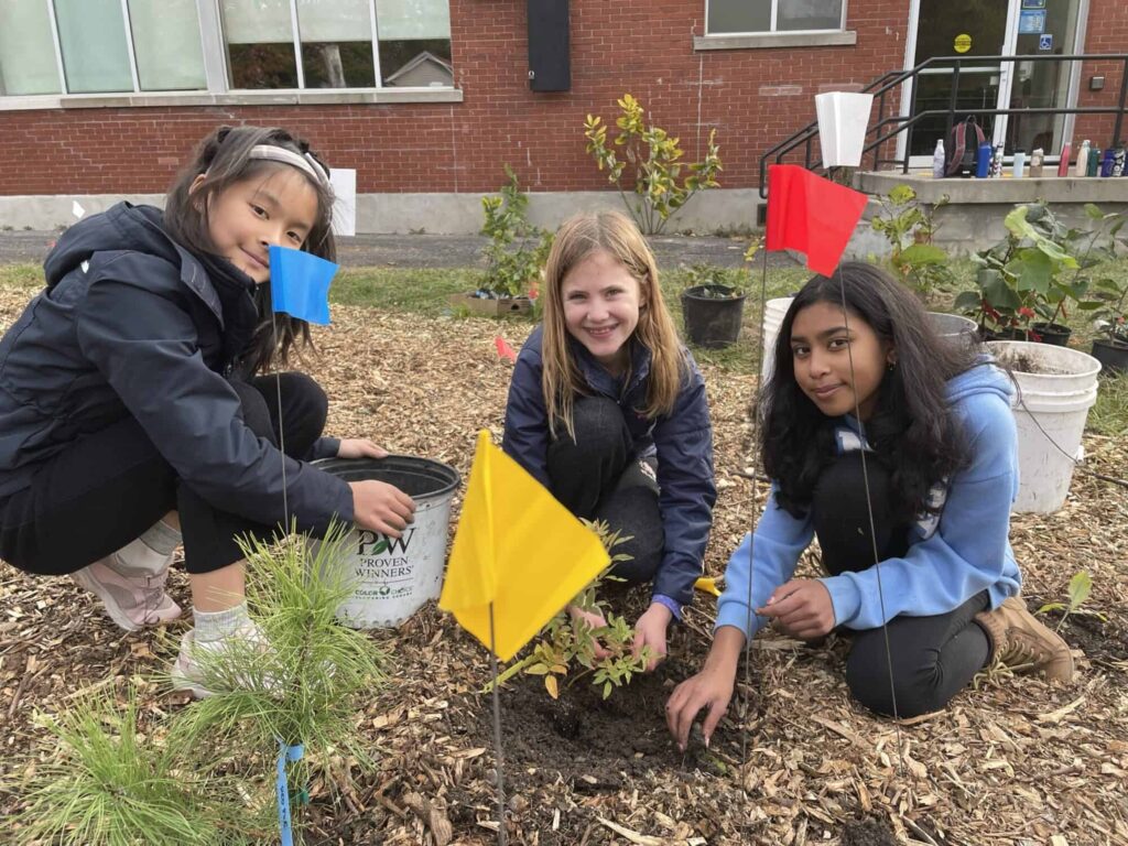 Children smiling and posing for camera while planting a mini forest.