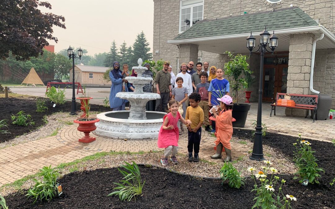 Men, women, and children pose in a straight line in front of the community mosque. The rain garden is in front of them.