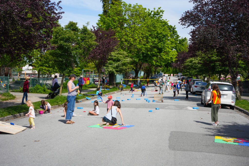 Children and adults partaking in various activities on a wide street.