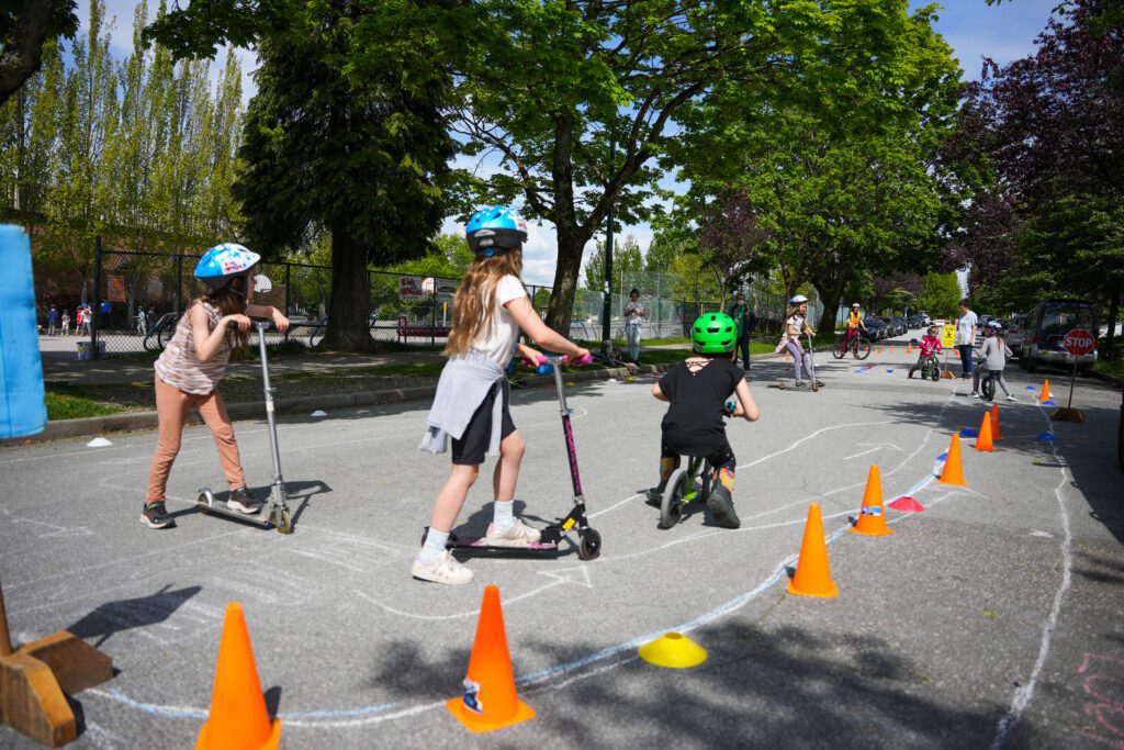 Children riding scooters in a sectioned off area of the street.