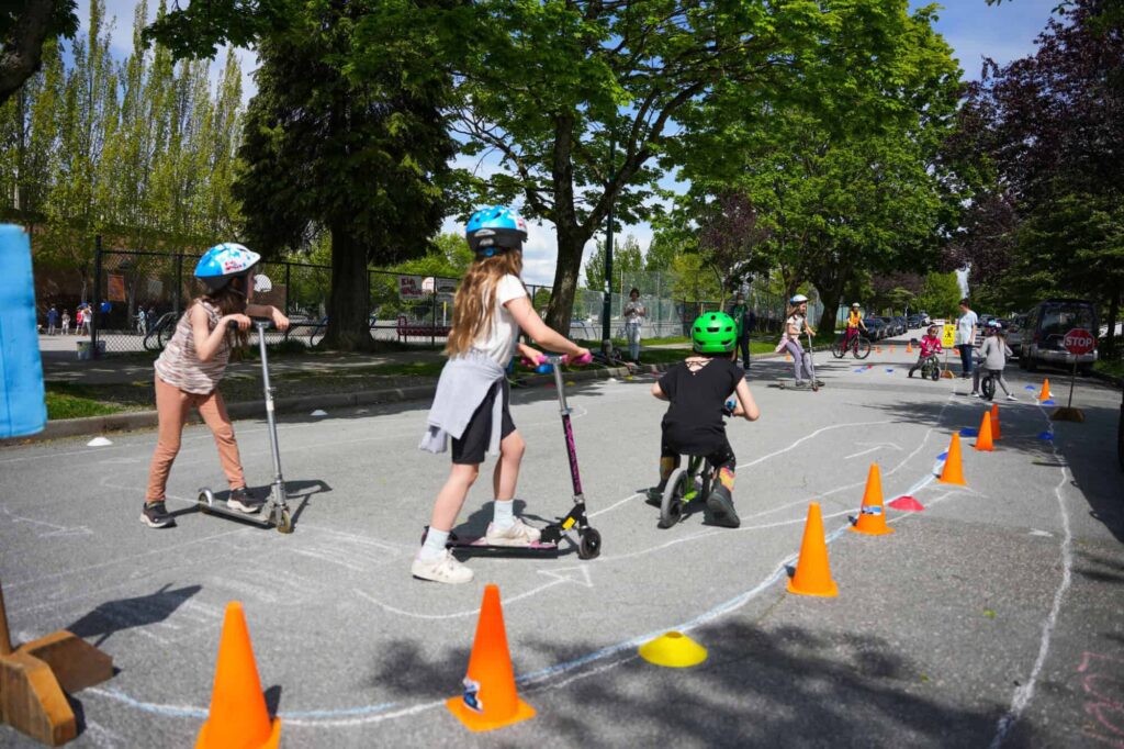 Children riding scooters in a sectioned off area of the street.