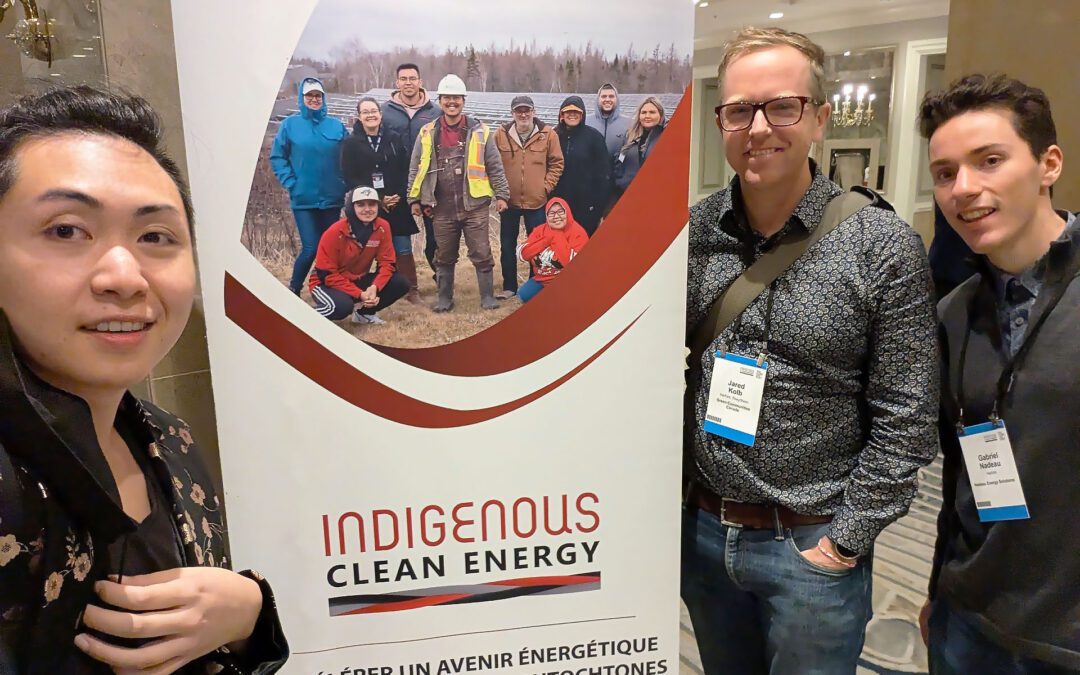 Instructed by the emcee, three attendees from Green Communities Canada pose in front of Indigenous Clean Energy Gathering banner.