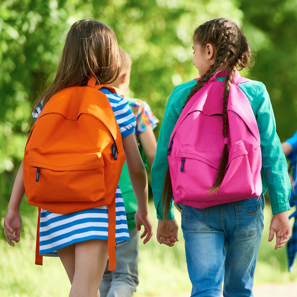 Two student girls walking with a larger group wearing brightly coloured backpacks