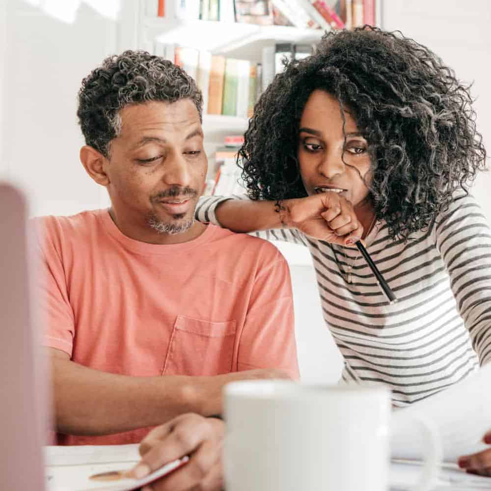 Couple looking at paper sitting in front of a computer screen