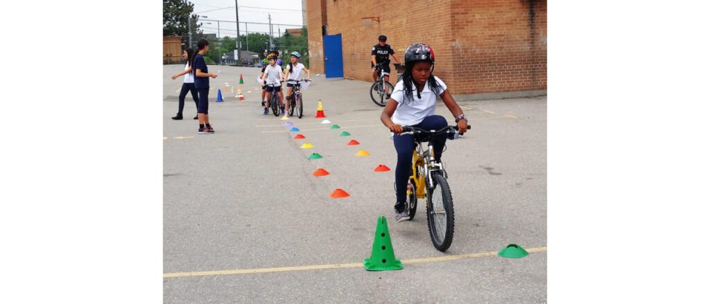 Group of kids participating in a cycling skills training session, each wearing helmets and riding bikes through a line of cones.