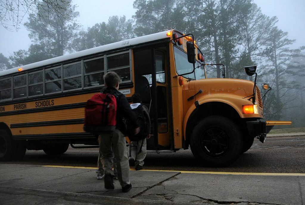 Children with backpacks board a yellow school bus parked on the roadside.