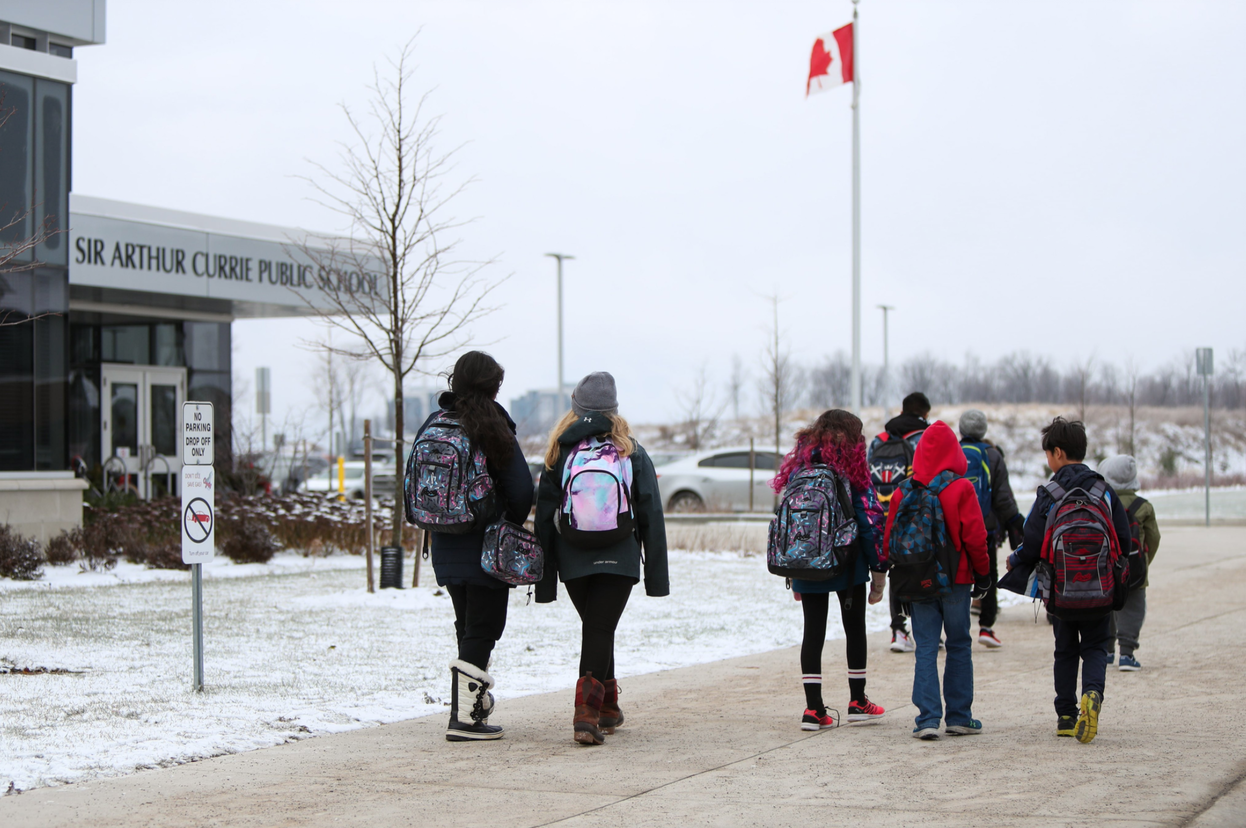 A group of students wearing backpacks walk toward a school building on a snowy day.