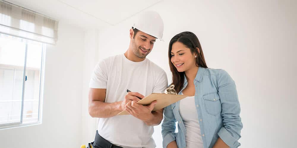 Woman and man wearing white hardhat looking at clip board.