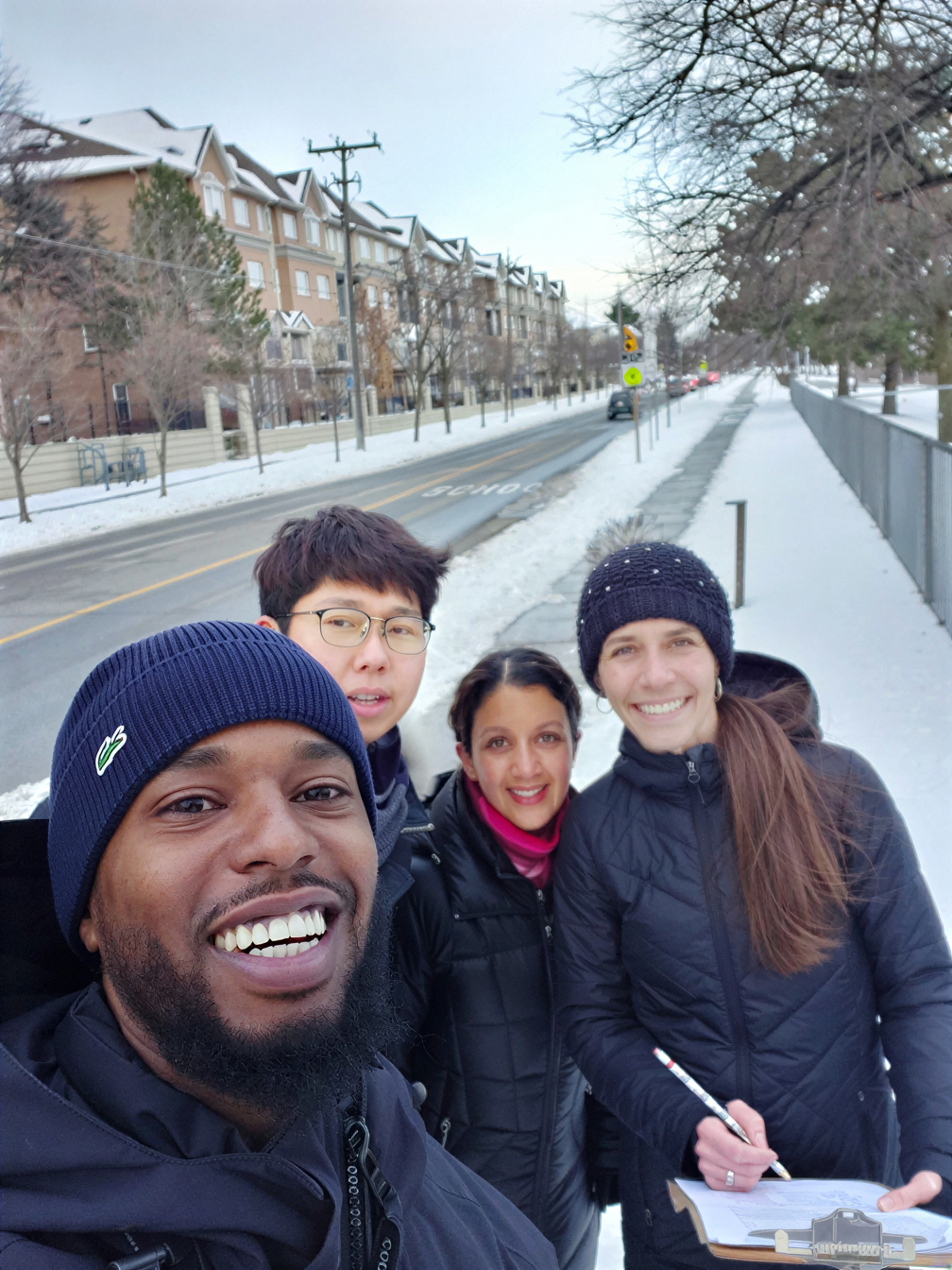 Four people outdoors on a snowy sidewalk smiling at the camera.