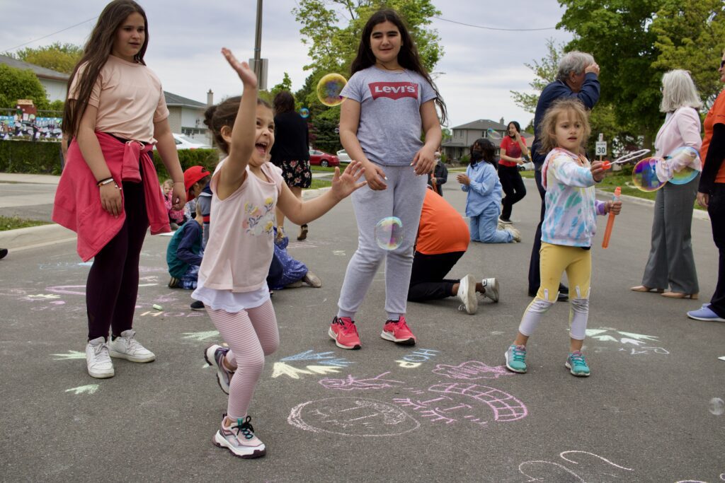 Children playing with bubbles and chalk drawings on a closed street during a School Street event.