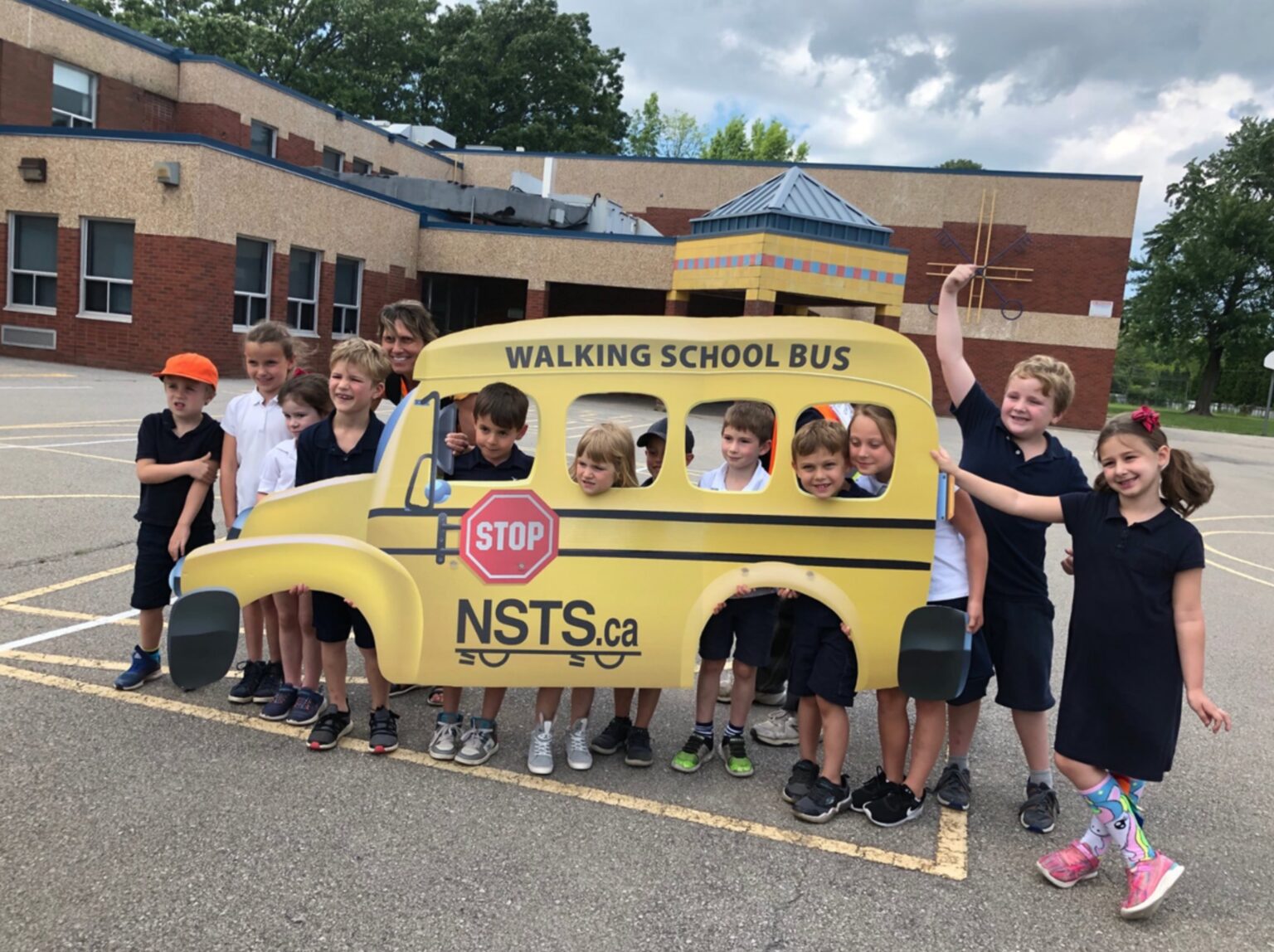 A group of children stand together holding a large cutout shaped like a school bus with the words “Walking School Bus.”