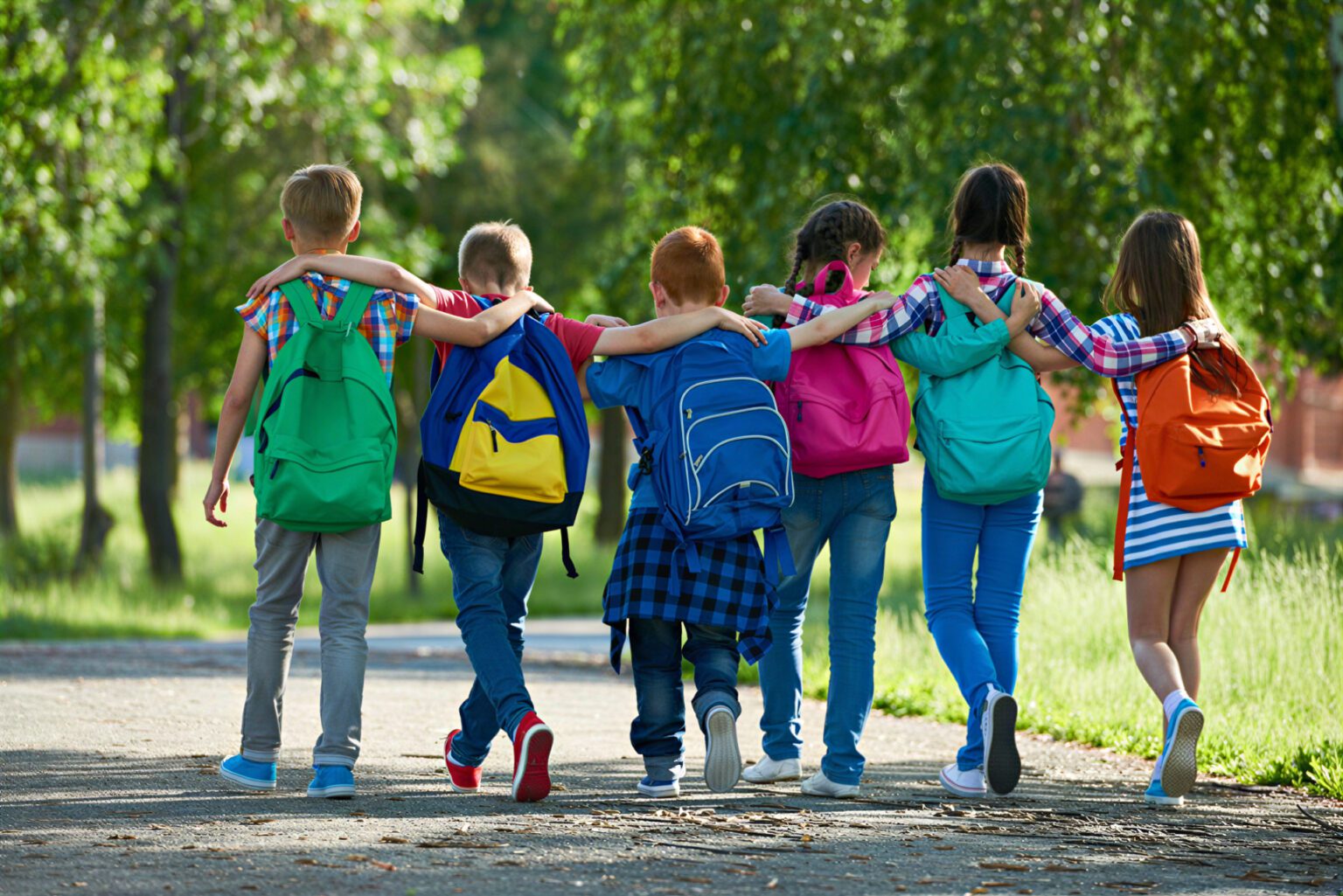 A group of children walking outside with their arms around each other’s shoulders.