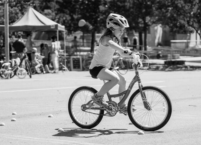 Child wearing a helmet rides a bicycle in an open, paved area.