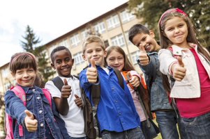 A group of smiling schoolchildren stand together outside, giving thumbs up.