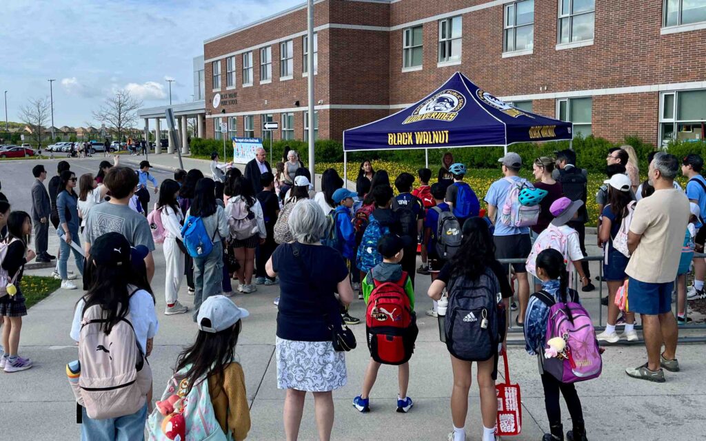 Dozens of children gather around an event tent on the pedestrianized street in front of Black Walnut Public School.