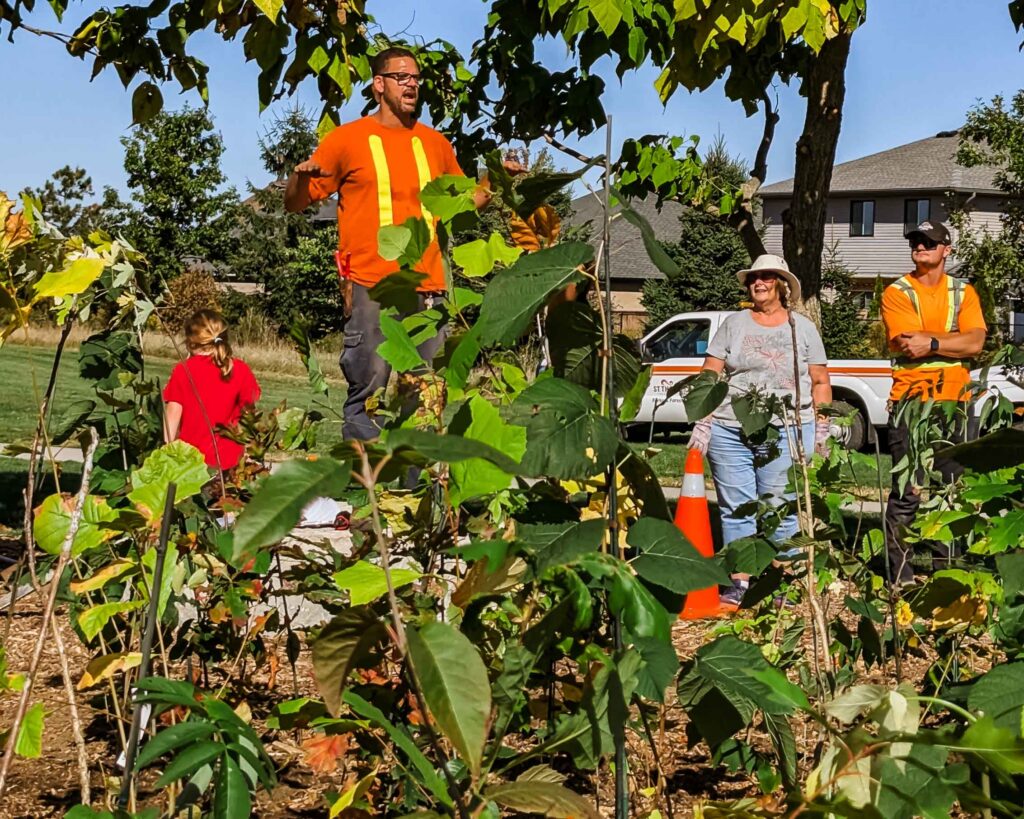This image shows volunteers at the mini forest planting site. A main volunteer is wearing a safety vest and providing instructions to the other participants.
