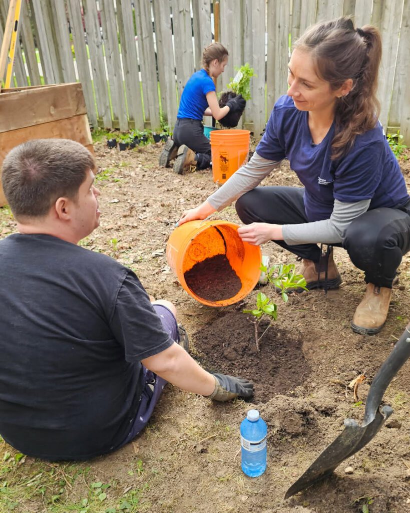 A volunteer helping a participant plant a native shrub in a community garden.