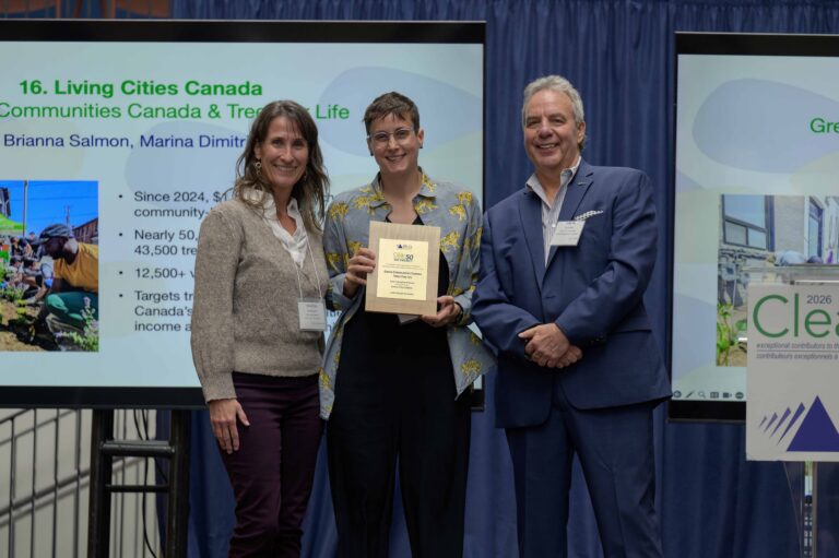 Three people on stage receiving award. Background screen identifies Living Cities Canada Fund, Green Communities Canada, and Trees for Life